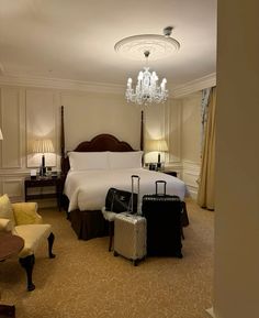 a hotel room with a bed, chandelier and suitcases on the floor