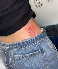 a woman's stomach with a red bow tattoo on her left side ribcage