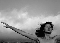 a woman with her arms outstretched in front of the ocean on a cloudy day,