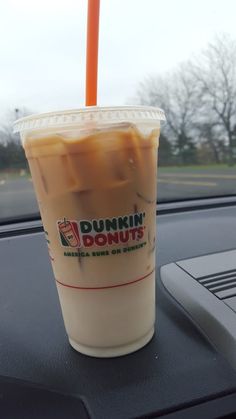 a dunkin donuts drink sitting on the dashboard of a car with an orange straw in it