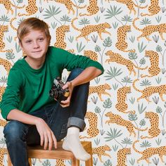 a young boy sitting on a stool with a camera in front of a wallpapered background