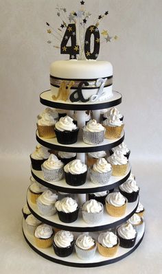 a tiered cake with white frosting and black icing, topped with cupcakes