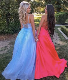 two women in long dresses standing next to each other on the grass with trees and bushes behind them