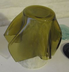 a green glass vase sitting on top of a white table next to two black rocks