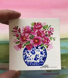 a hand holding up a card with flowers in a blue and white vase on it