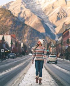 a woman is walking down the street in front of some snow covered mountains and buildings