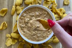 a hand holding a tortilla chip over a bowl of dip