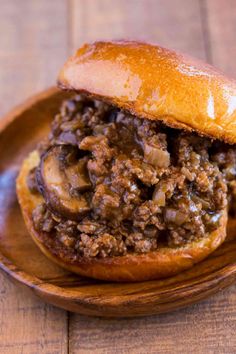 a close up of a sandwich on a wooden plate with meat and mushrooms in it