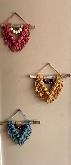 three crocheted necklaces hanging on a wall with hooks and string attached to them