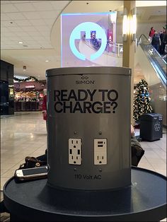 a black trash can sitting on top of a table in a shopping mall next to an escalator