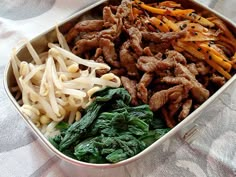 a metal container filled with pasta and meat next to spinach leaves on a table