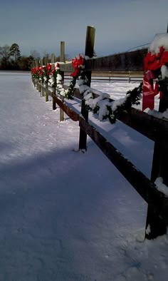 a wooden fence covered in snow with red bows on it's posts and wreaths