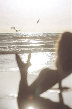 a woman sitting on top of a beach next to the ocean with birds flying overhead