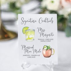 a sign with cocktails on it sitting on a table next to flowers and candles