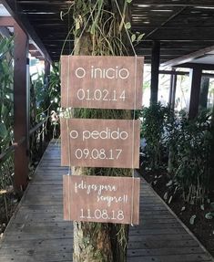 a wooden sign hanging from the side of a tree in front of a walkway covered with plants