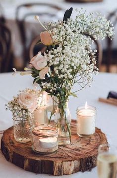 flowers and candles are arranged in mason jars on a wood slice at a wedding reception