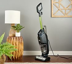 a vacuum is on the floor next to a lamp and potted plant in a room