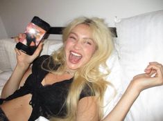 a woman laying in bed holding up a cell phone