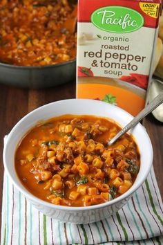 a bowl of red pepper and tomato soup next to a carton of organic pasta