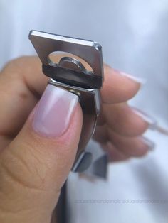 a woman's hand holding a metal ring with pink and white nail polish on it