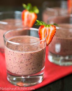 three glasses filled with smoothie and strawberries on a red cloth next to each other