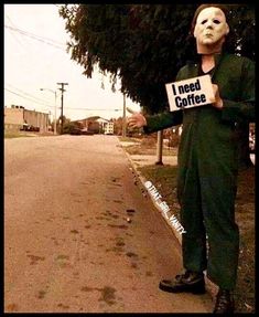 a man wearing a mask holding a sign that says i need coffee