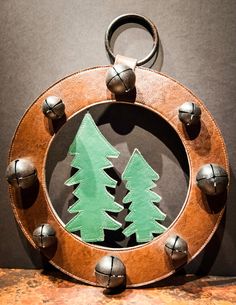 a metal and wood christmas ornament with green trees on it's side