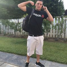 a man standing in front of a white picket fence talking on a cell phone and holding his hand up to his ear