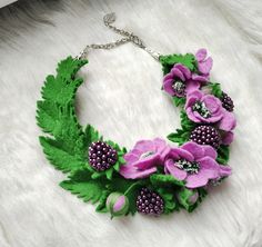 a green and purple flower necklace on a white furnishce background with beads, leaves and berries