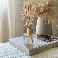 reeds in a glass bottle next to a book on a white tablecloth with a vase