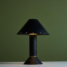 a black lamp on a white table with a green wall in the backround