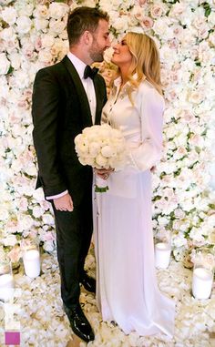 a man and woman standing next to each other in front of a flower covered wall