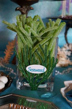 a glass vase filled with green plants on top of a table