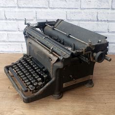 an old fashioned typewriter sitting on top of a wooden table next to a brick wall