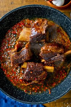 a bowl filled with meat and sauce on top of a wooden table next to a blue towel