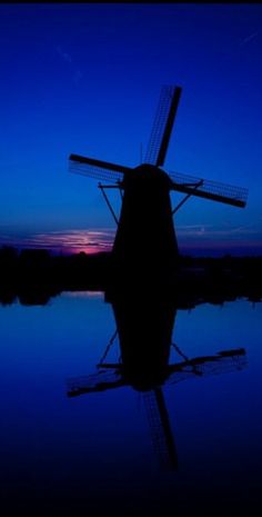 a windmill sitting on top of a body of water at night with the sun setting behind it