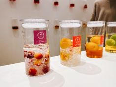 four glasses filled with different types of drinks on a table next to a woman in a gray sweater