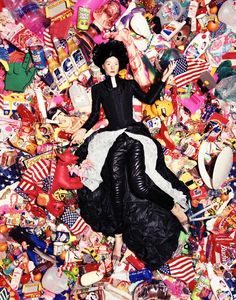 a woman in black dress surrounded by lots of toys and confetti on the floor