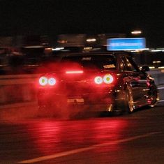 a car driving down the road at night with its lights on and fog coming from behind it