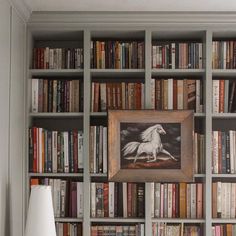 a bookshelf filled with lots of books next to a lamp and painting on the wall