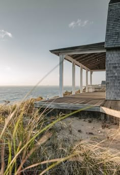 a house sitting on top of a sandy beach next to the ocean with grass in front of it