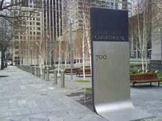 a sign that is on the side of a sidewalk in front of some trees and benches