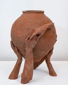 a large clay pot with two hands on it's face and one hand over the other