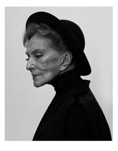 an old woman wearing a hat and black coat with her eyes closed, looking off to the side