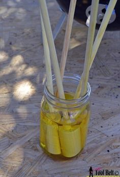 a jar filled with yellow liquid sitting on top of a wooden table next to a grill