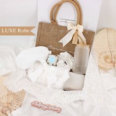 a white bed topped with lots of items next to a brown bag and some straw hats