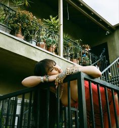 a woman leaning on a railing in front of a building with potted plants behind her