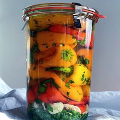 a jar filled with lots of vegetables on top of a white table covered in cloth