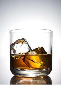 a glass filled with ice sitting on top of a reflective table next to a white wall