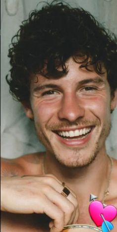 a man with curly hair smiling and holding a heart shaped object in his right hand